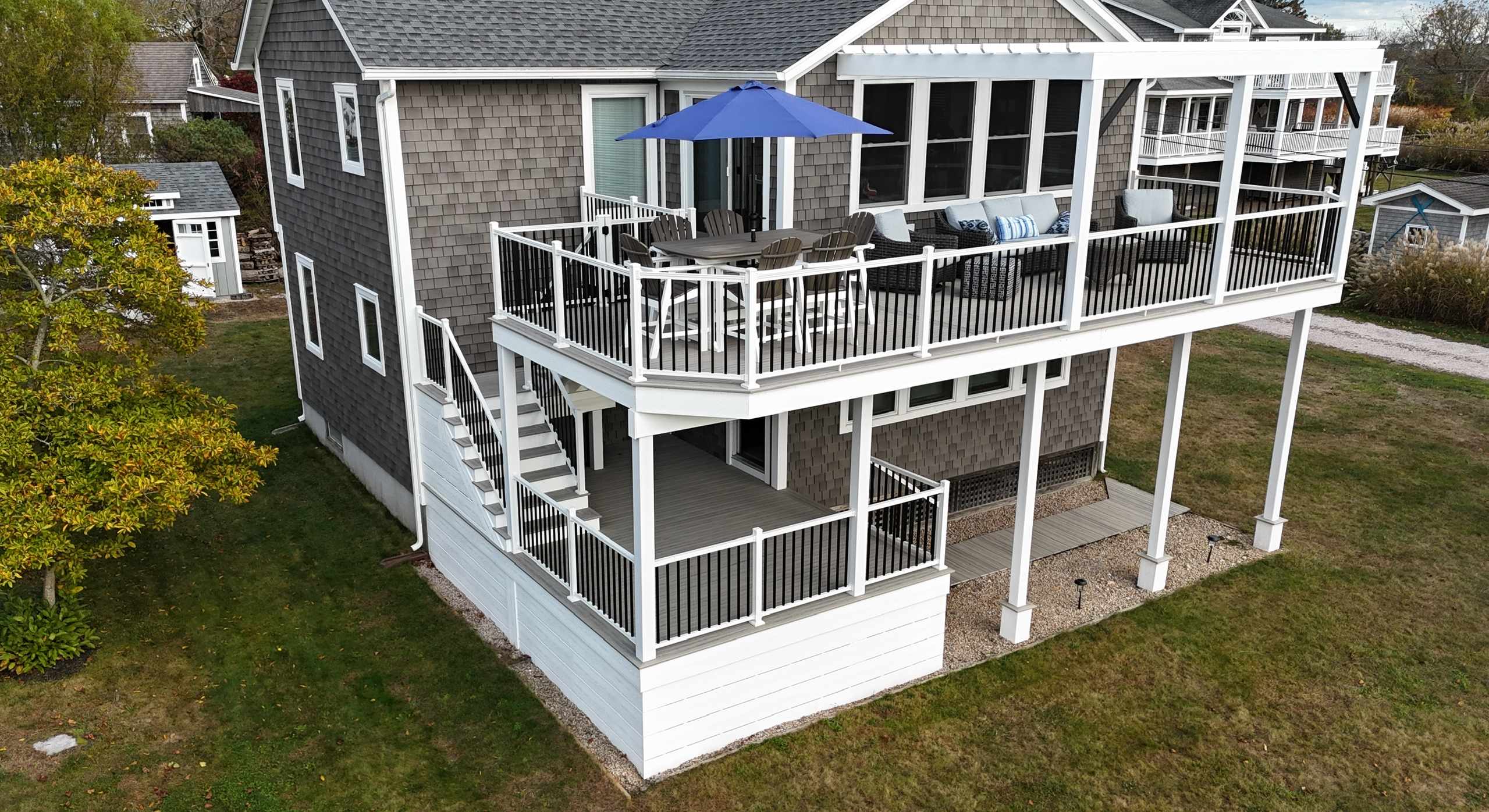 Two-story home with an elevated wraparound deck featuring white railings, outdoor seating, and a blue patio umbrella.