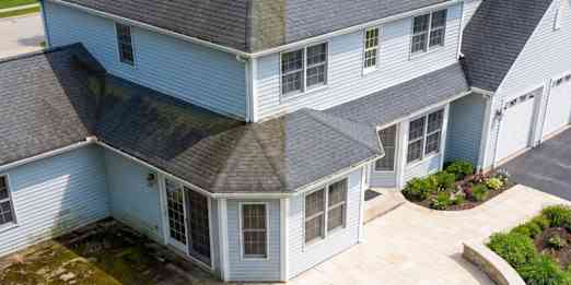 Grey house with grey roofing shingles with half showing "before" and "after" cleaning the roof.