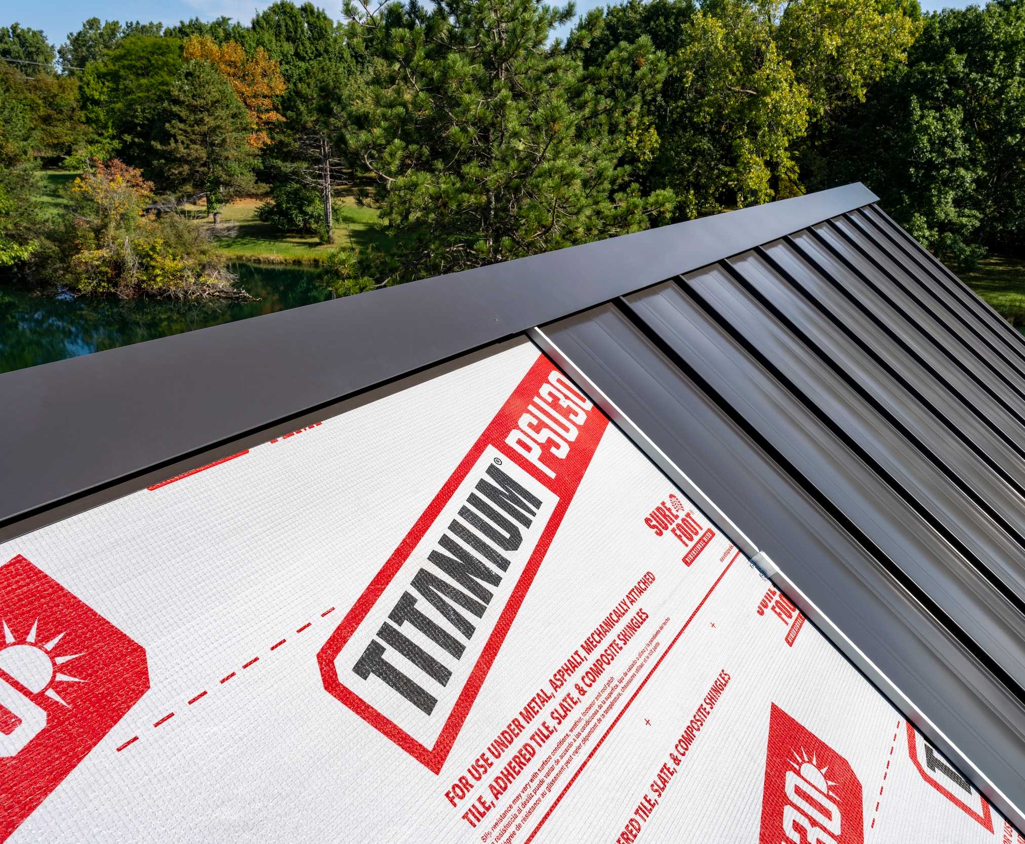 Close-up of a dark metal roof installation over TITANIUM® PSU30 roofing underlayment, with trees in the background.
