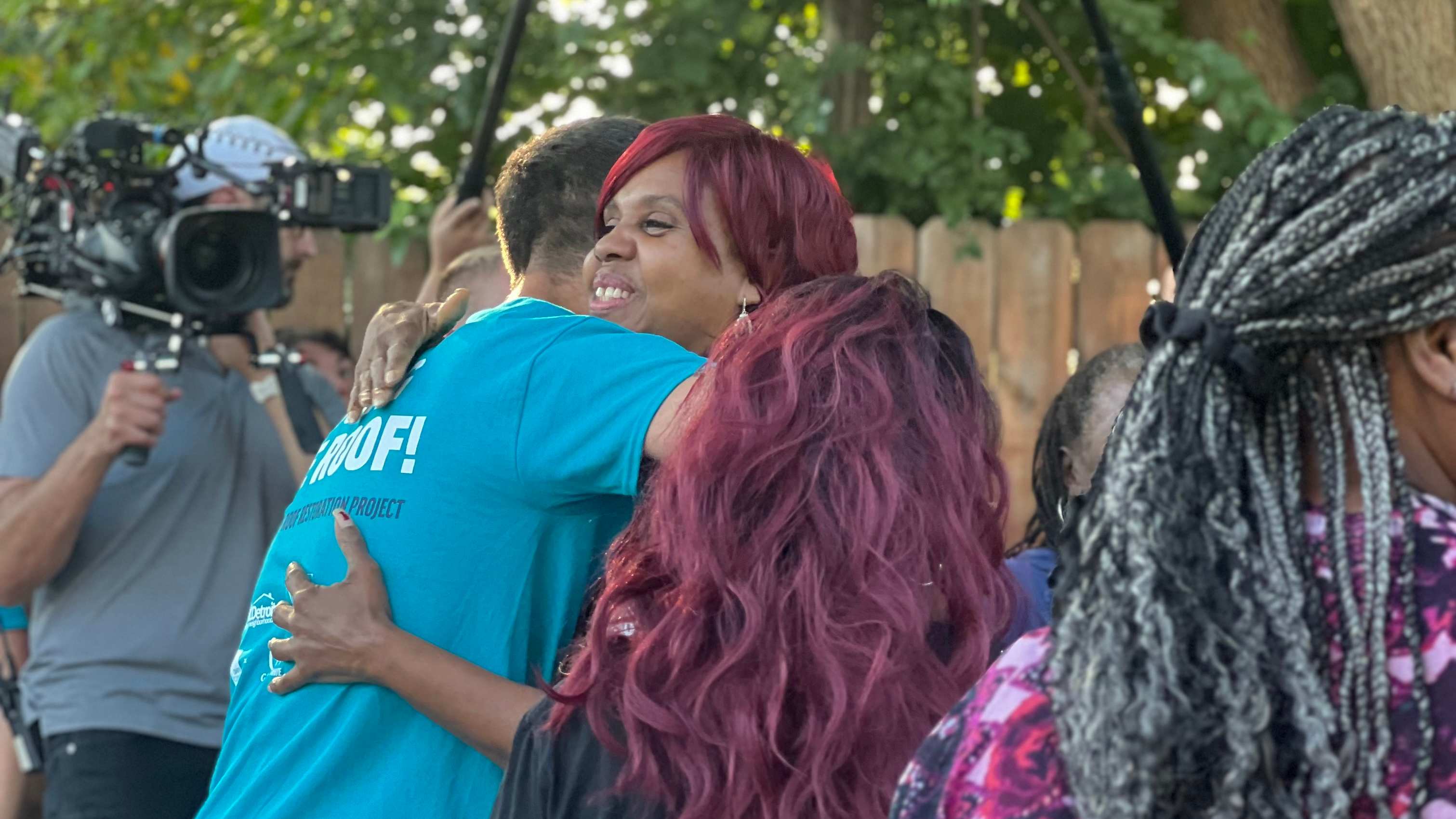 Happy homeowners hug Evan with Bargain Block camera crews in background.