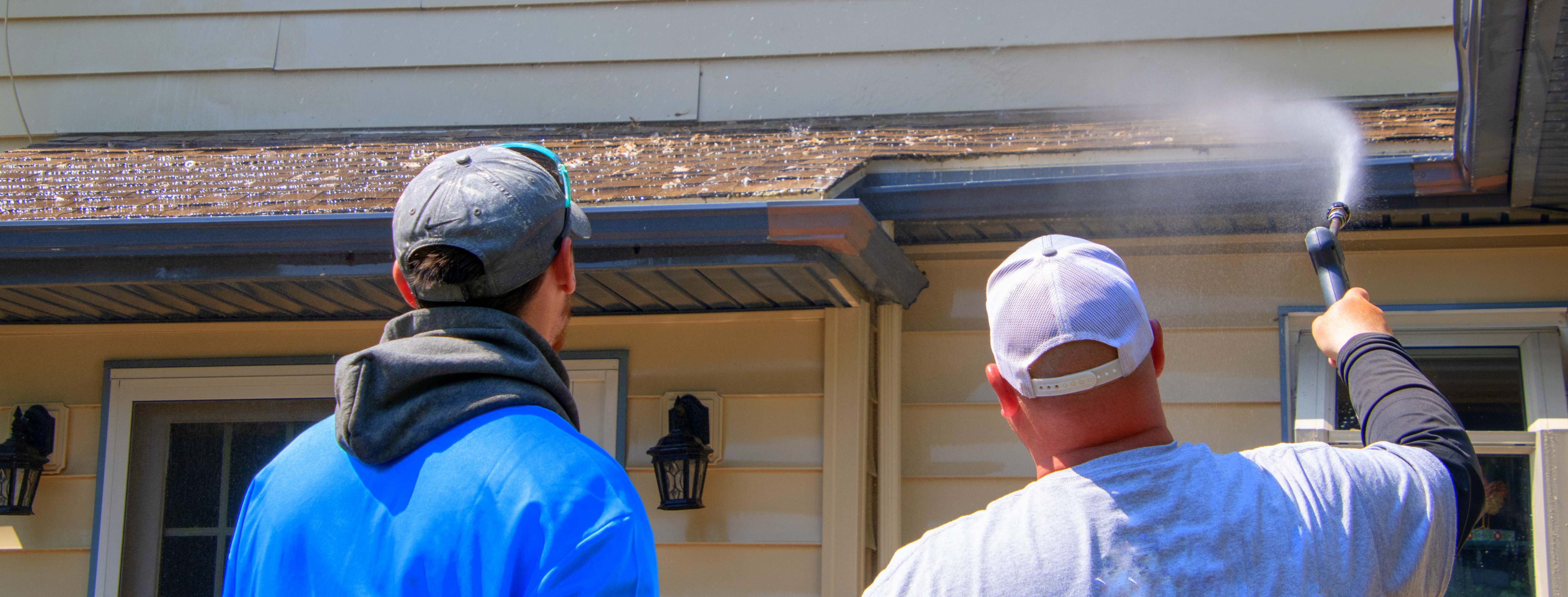 Homeowners spraying off roof shingles with a garden hose.