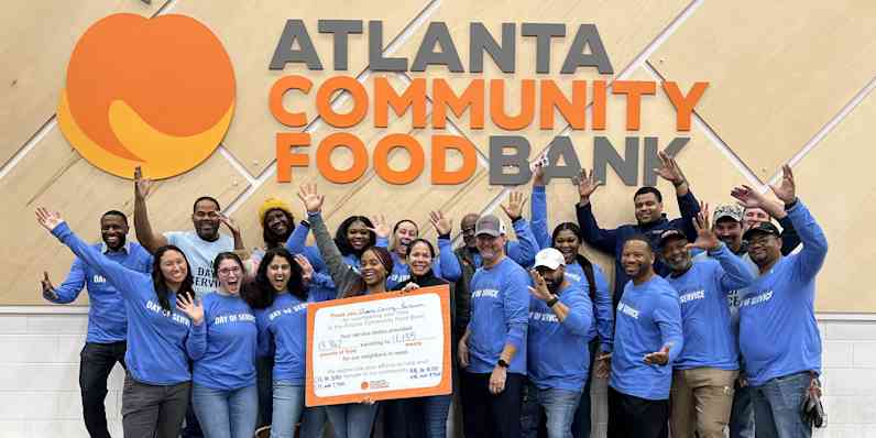 Photo of our Atlanta plant smiling while staning together in blue shirts in frotn of an orange sign that reads "atlanta community food bank"