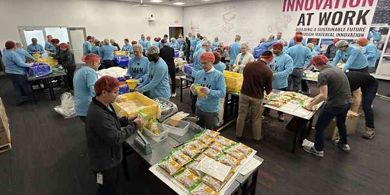 Photo of people wearing blue shirts working together to assemble food wearing food safety hats