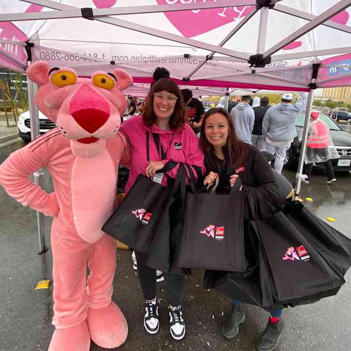 La mascota de la Pantera Rosa de pie con dos empleados de Owens Corning sosteniendo bolsas de supermercado reutilizables negras con el logotipo de Owens Corning.
