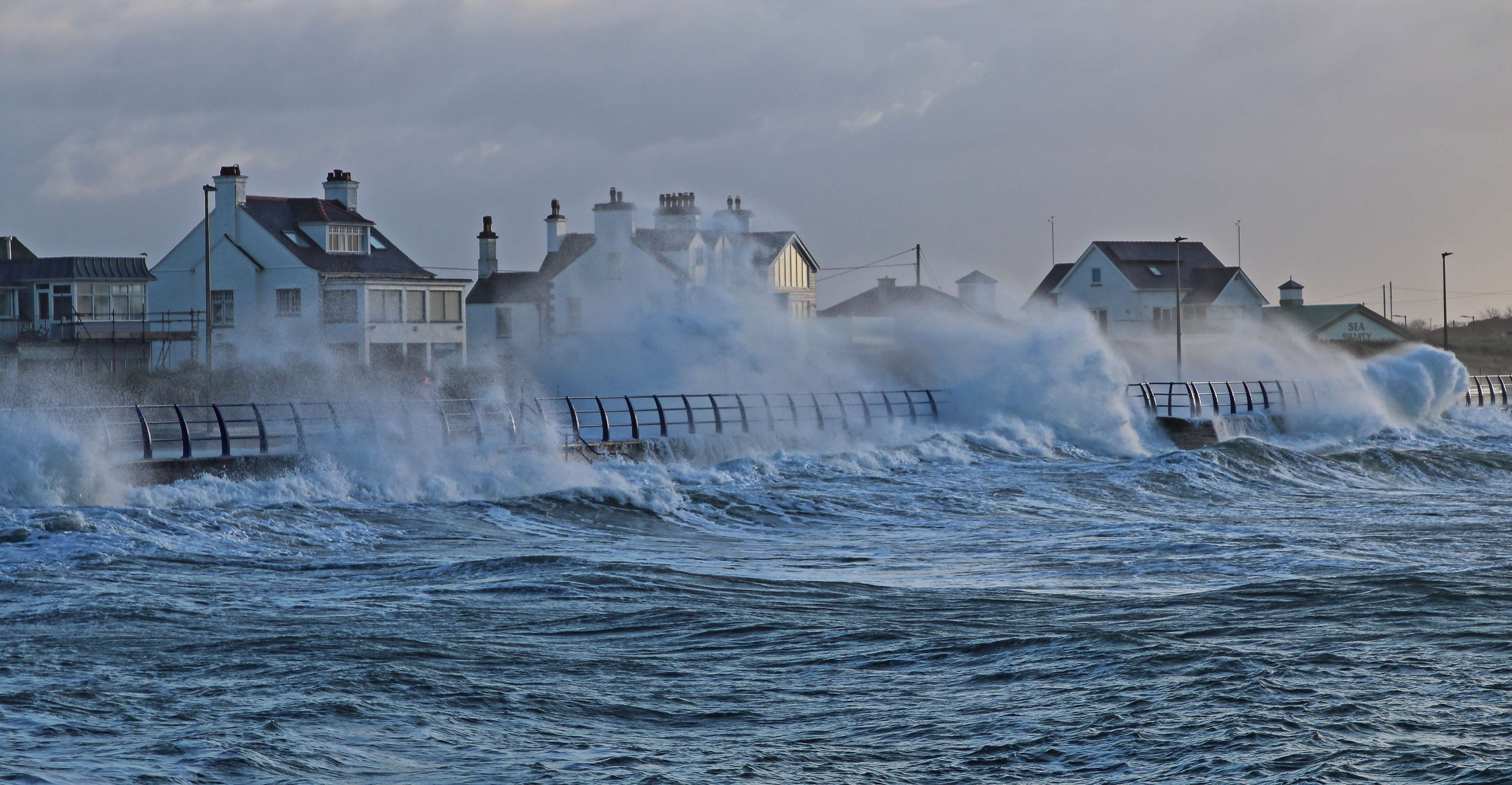 Photo of stormy ocean waters crashing into docks and houses on the coast