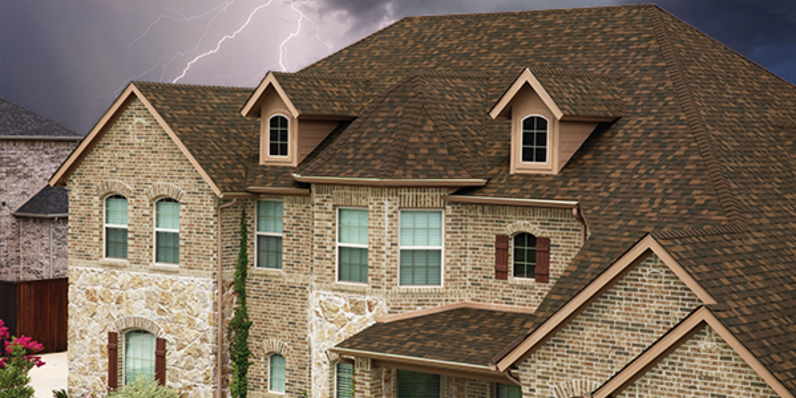 Tan brick home with Owens Corning Duration FLEX shingles in Brownwood in front of a stormy sky with lightning.