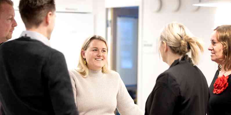 Flere kolleger fra Paroc står rundt et bord i et kontormiljø og prater.