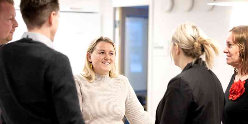 Flere kolleger fra Paroc står rundt om et bord i et kontormiljø og snakker.