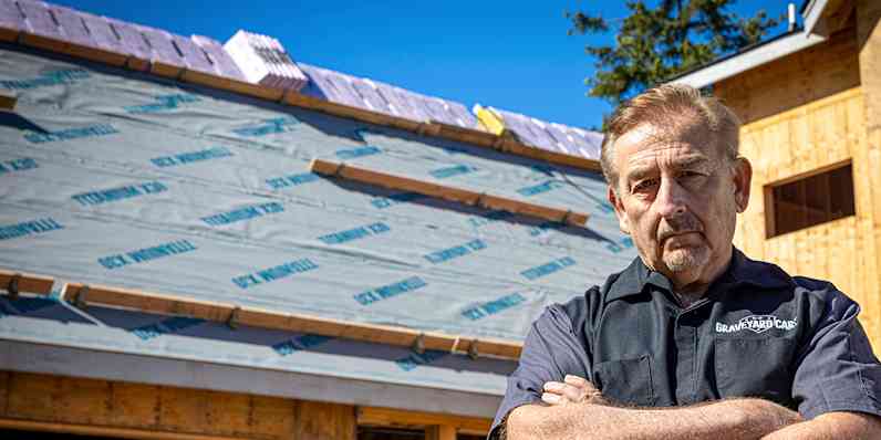 Mark Worman standing with his arms crossed in front of his in-construction dream home with underlayment spread across the roof