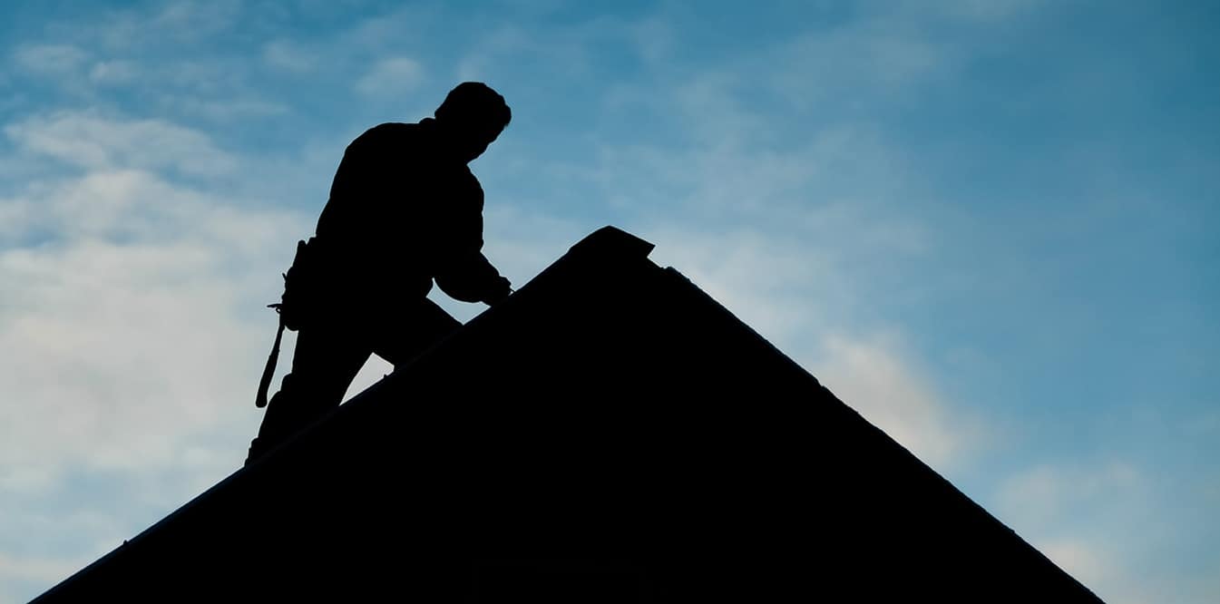 Silhouette of contractor on a roof peak.