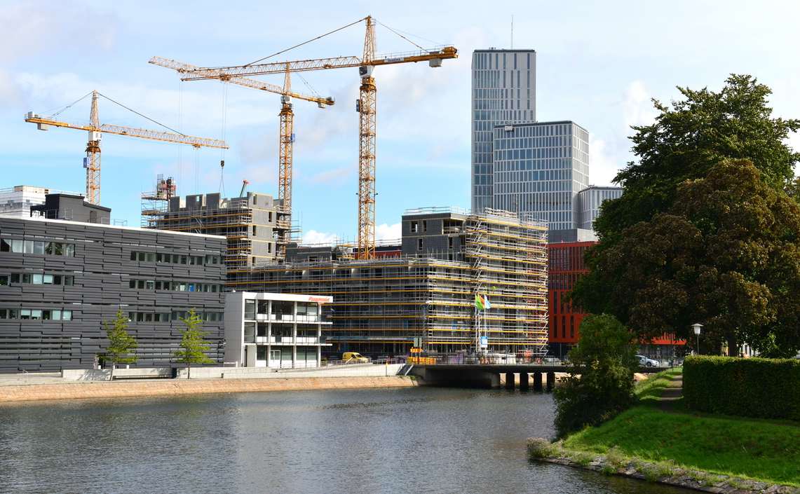 en rekke bygninger under oppføring på elvebredden og byggekraner i bakgrunnen