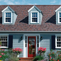 Blue grey house with Owens Corning Duration Designer shingles in Merlot, surrounded by a blue sky and shrubbery with spring flowers.