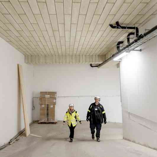 Två personer går i ett parkeringsgarage där PAROC CGL 20cy Undertakslameller är installerade.