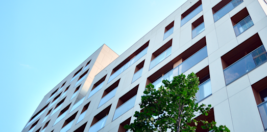 A white building with ventilated facade is seen from beneath with a light blue sky in the background.