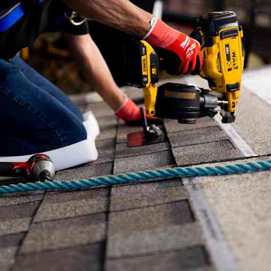 Close up of a contractor using a nail gun to install shingles