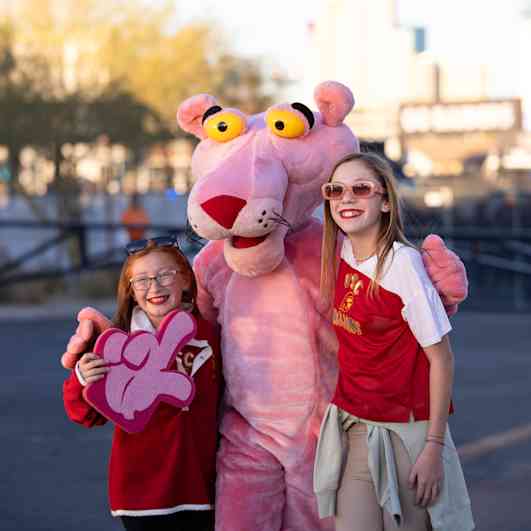 The Pink Panther mascot standing with his arms around two girls holding a foam finger.