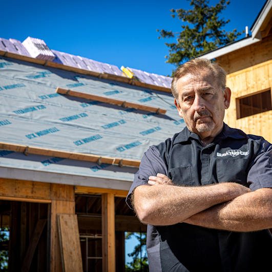 Mark Worman stands with his arms crossed in front of his home that has underlayment installed on the roof deck