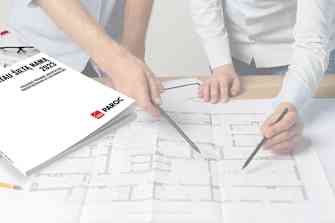 katalogas "statau šiltą namą", gulintis ant stalo kartu su liniuotėmis ir brėžiniais, prie stalo stovi du vyrai ir rodo į brėžinius