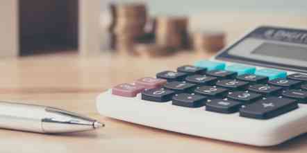 Closeup photo of a calculator sitting on a desk alongside a pen