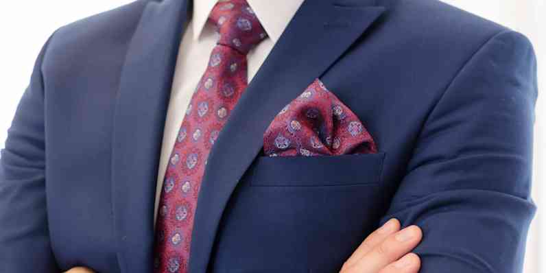 Photo zoomed in on the chest of a man wearing a navy blue suit with red patterned tie
