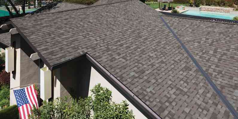 Photo of the top of a roof with COOL shingles installed, with green grass and a pool in the background