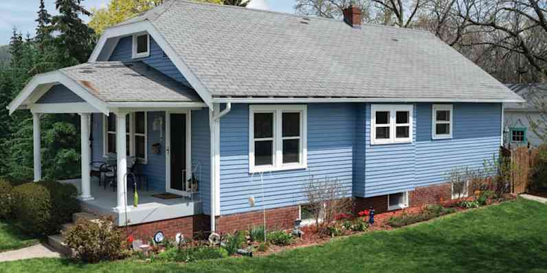 Blue craftsman style house with white windows and old, worn grey roof.