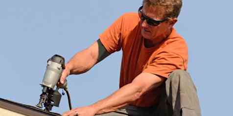 Photo of a homeowner working on top of their roof installing shingles