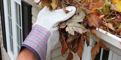 gloved hand removing leaves from white gutters on a red roof