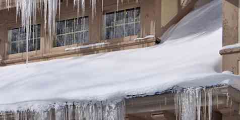Photo of the roof of a house covered with snow, with icicles hanging