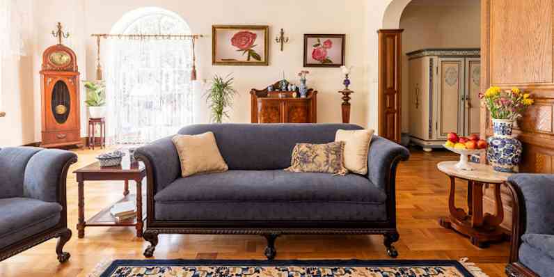 Cobalt blue sofa and other antique furniture on a wooden floor in a spacious living room interior of a classic mansion.