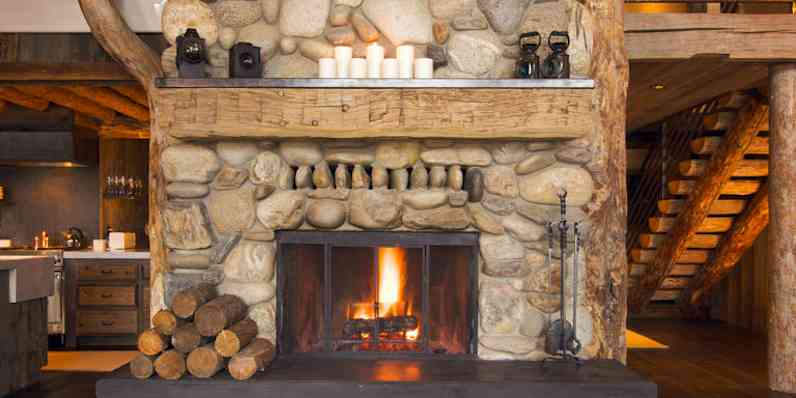 A rustic scene with a stone fireplace running, with logs by the fire
