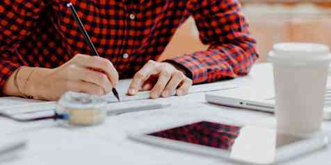 Photo of a person sitting at a desk in front of a laptop taking measurements on a large sheet of paper