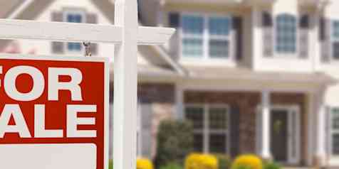 Photo of a red "For Sale" sign in the foreground, with a two story home in the background