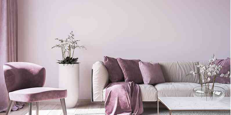 Livingroom with pale purple walls, Purple chair and light colored couch with different purple shades of throw pillows.