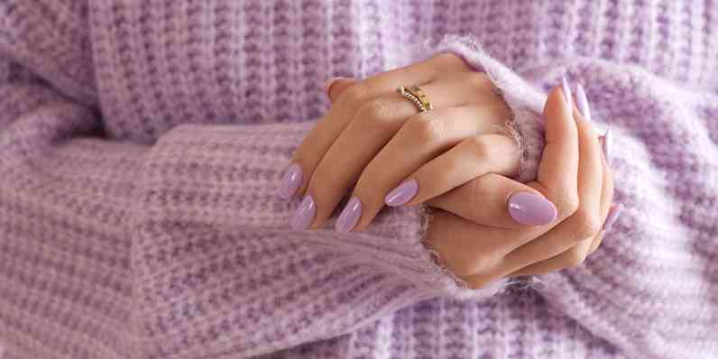 Woman wearing a light purple cable knit sweater with hands cradled with light purple nails.