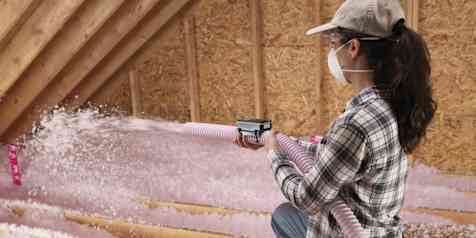 Woman installing AttiCat® blown-in, loose fill insulation covering joists
