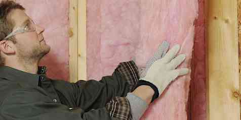 Man in green shirt installing unfaced insulation in 2 by 6 wall studs