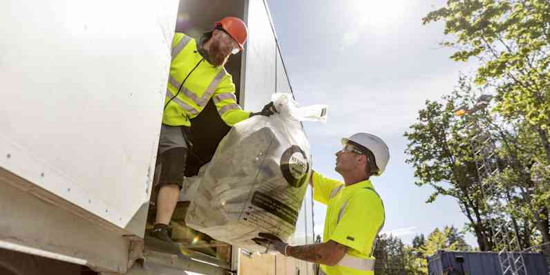 two make workers unloading used stone wool from a truck for recycling