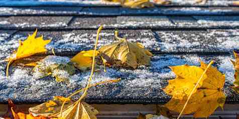 Close up view of shingles with snow and frost coating, and fall leaves.