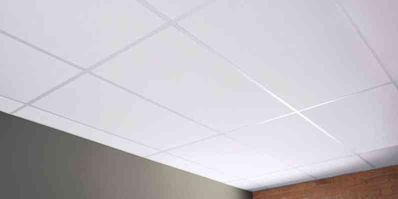 White ceiling veil tiles installed in the ceiling of a room with a brick wall. 