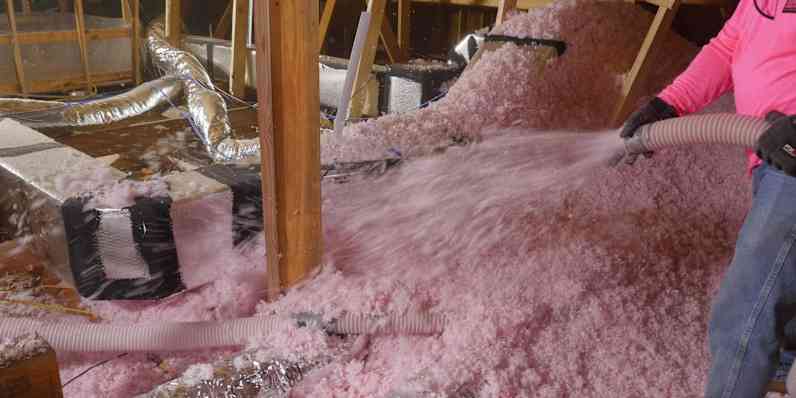 Partially insulated attic with insulation being blown in around ducts