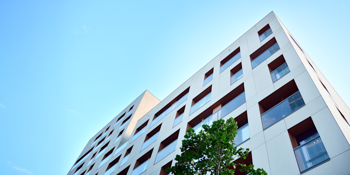 A white building with ventilated facade is seen from beneath with a light blue sky in the background.