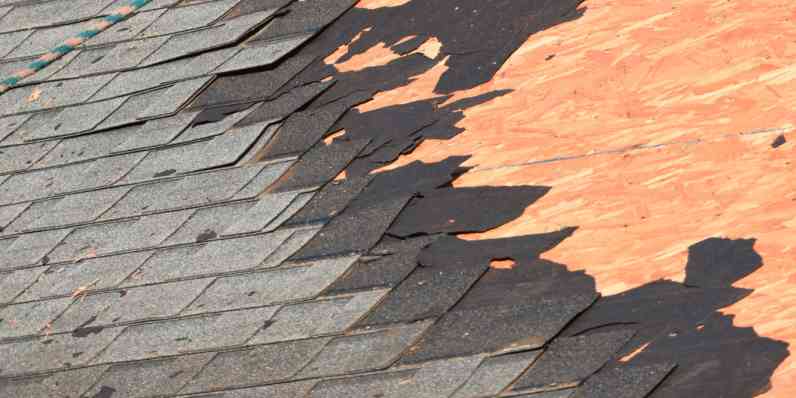 Shingles being torn off a roof showing the wood decking underneath.