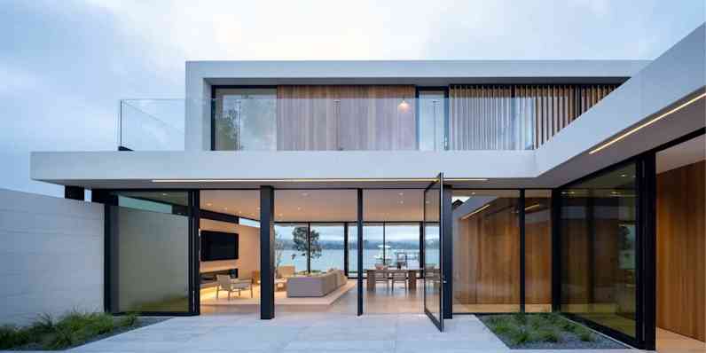 Exterior view of a modern building with open glass doors and windows, overlooking a water-front view.