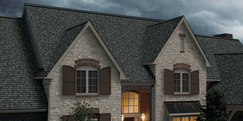 A tan brick home with Duration STORM shingles in Estate Gray with a grey stormy sky overhead.