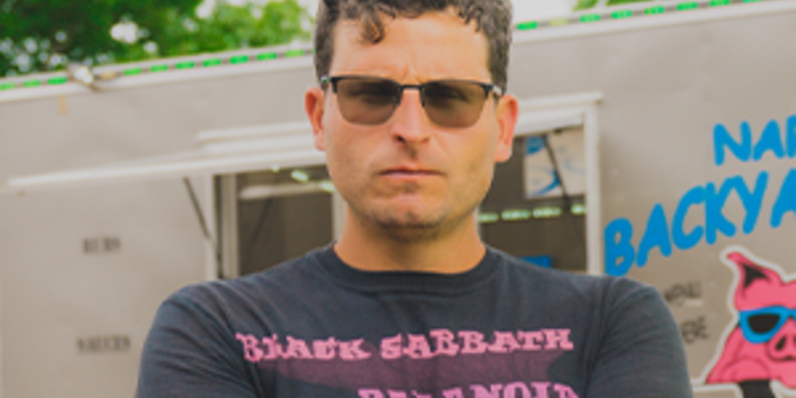 Person wearing a Black Sabbath Paranoid T‑shirt standing outdoors near a trailer with colorful graphics.