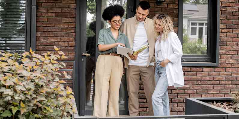 Homebuyers standing in front of brick home reviewing documents with real estate agent,