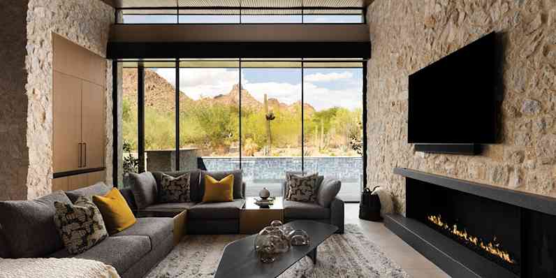 Modern living room with couches, tv, fireplace, and a wall of windows overlooking the water.