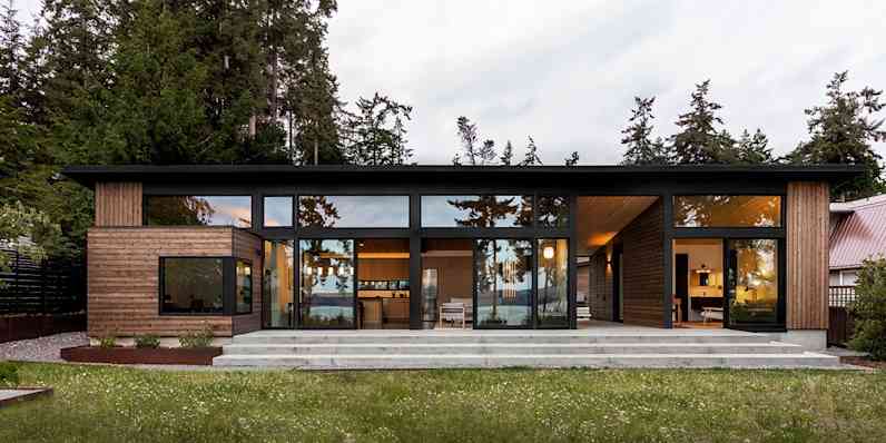 Outside view of a modern home with floor-to-ceiling windows, nestled among pine trees.