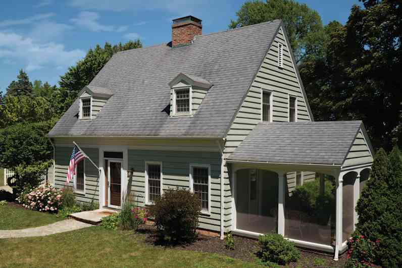 Foto de una casa de color verde claro con tejas grises más viejas y teñidas